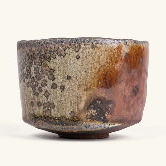A handmade ceramic tea bowl with a rustic, hand-painted glaze featuring mottled brown, beige, and black patterns, set against a plain beige background.